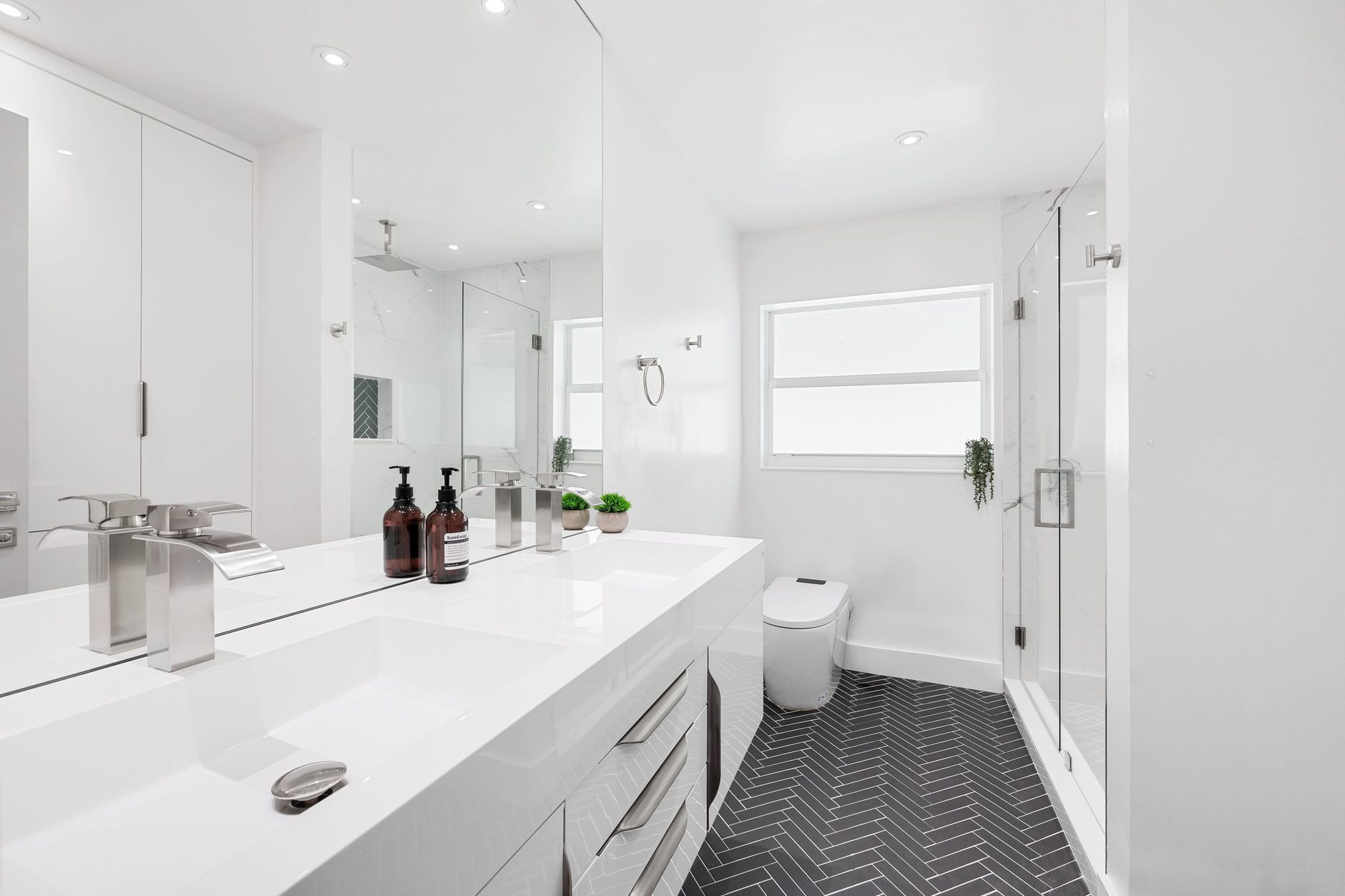 Modern white bathroom featuring sleek fixtures and herringbone flooring design in Riverside, CA